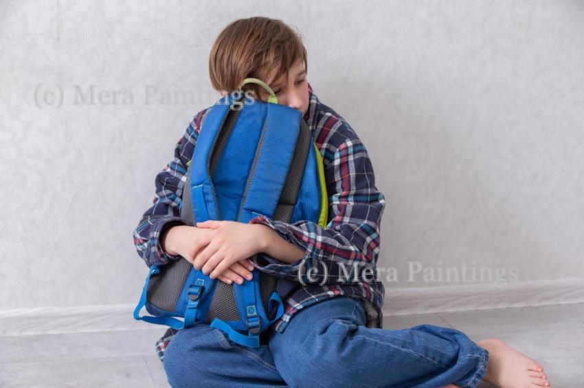 A child sitting on the floor, hugging a blue school backpack in a cozy room in the afternoon. He is tired of studying.