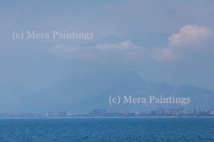 A landscape with a blue sea and a city blurred in the distance near a mountain.